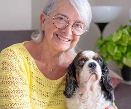 An elderly woman in a yellow top is holding a dog.