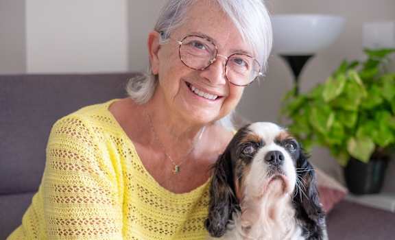 An elderly woman in a yellow top is holding a dog.