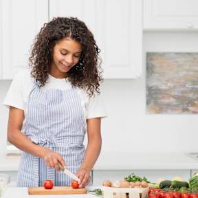 A woman in a striped apron is cutting vegetables on a cutting board.
