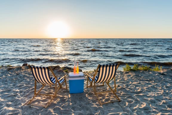 two beach chairs and a drink on the beach at sunset