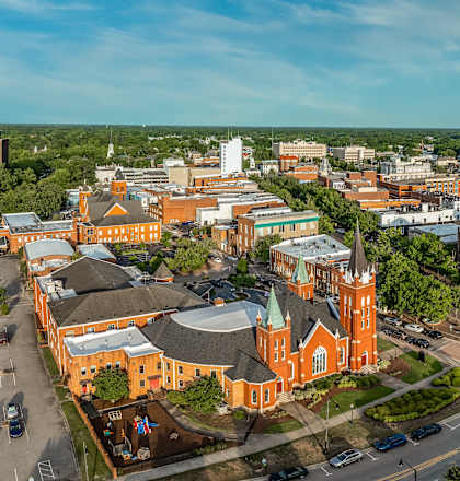 A large building with a green dome is surrounded by other buildings and trees.