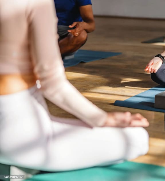 A group of people are sitting in a circle on yoga mats, meditating.