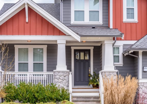 a gray house with a red door and a white porch