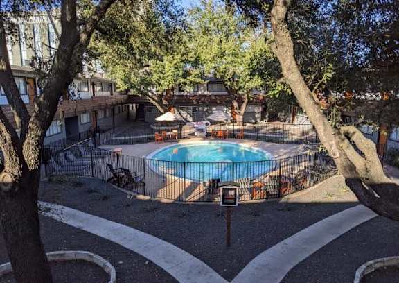 A pool surrounded by trees and a white fence.
