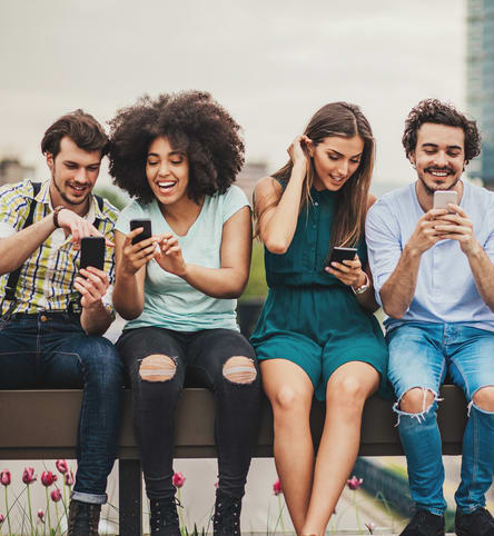 a group of people sitting on a bench looking at their cell phones