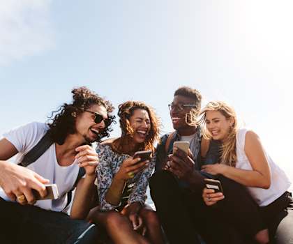 a group of friends sitting on a rock looking at their cell phones at Promontory, Tucson, AZ
