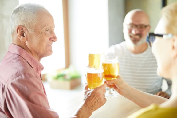 an older man and woman holding up glasses of beer while sitting at a table
