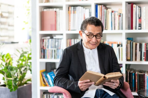 an older man sitting in a chair in front of a bookshelf reading a book