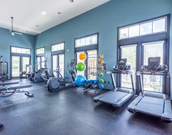 a large fitness room with cardio equipment and windows