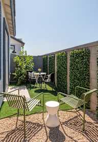 A patio with a white vase, green chairs and a table.