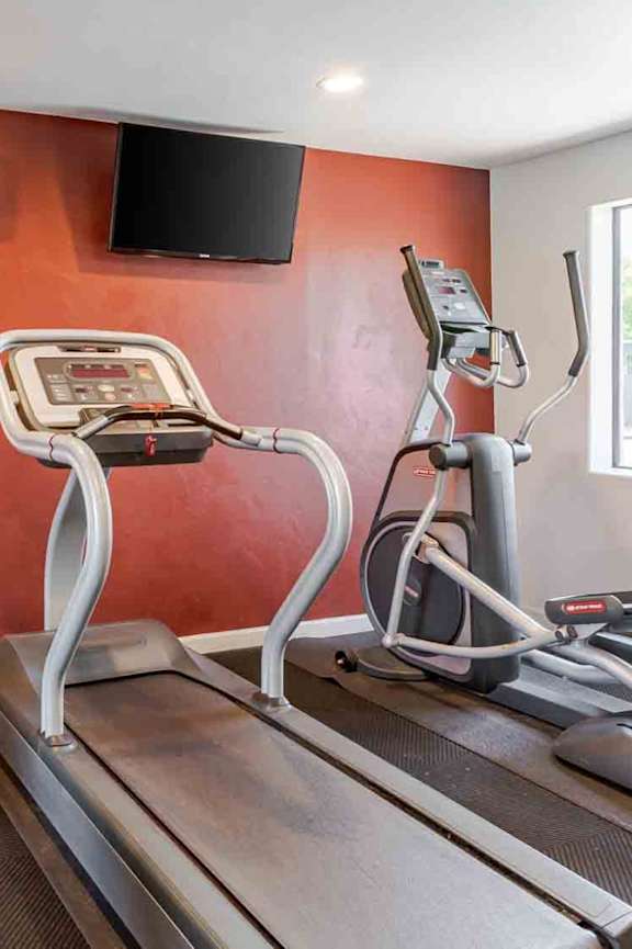 A treadmill with a monitor and a television on the wall.