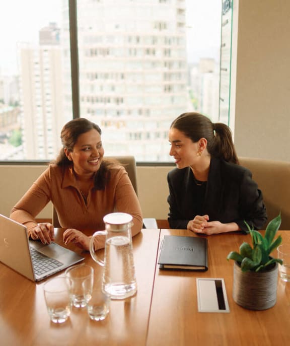 two women sitting at a table with laptops