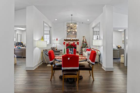 A Christmas tree with red and green decorations is in the middle of a room with a dining table and chairs.