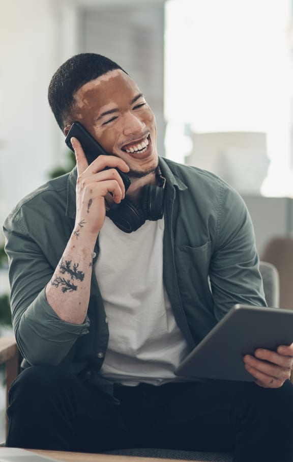 a man sitting in a chair talking on the phone and holding a tablet