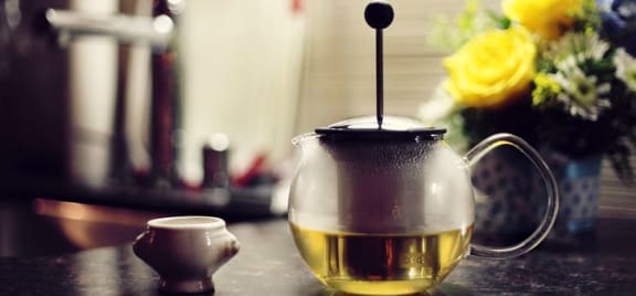 a glass teapot with a cup of tea on a table