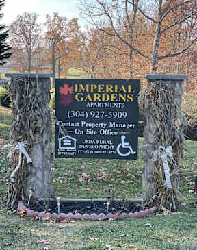 A sign for Imperial Gardens apartments is displayed in front of a tree.