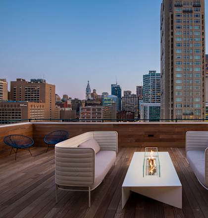 A rooftop patio with a table and chairs overlooking a city skyline at dusk.