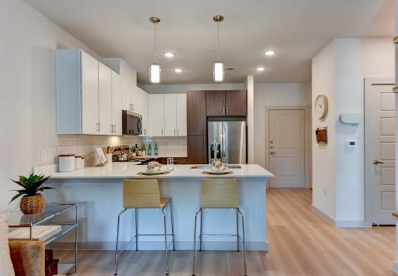A kitchen with a white counter and bar stools. at Bridge at Saffron, Austin, TX 78717