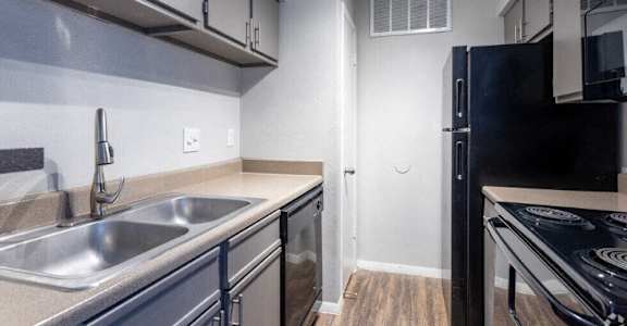 A black refrigerator stands in a kitchen with a stove top oven to the right.