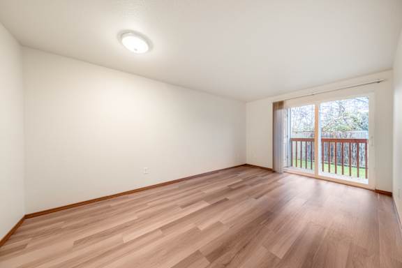 A room with wooden flooring and a window with a view of a fence.
