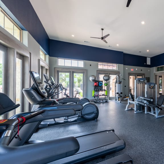 a gym with cardio equipment and weights on the floor and windows