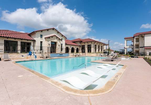 a swimming pool with chairs and a building in the background
