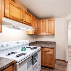 A kitchen with a white stove top oven and wooden cabinets.