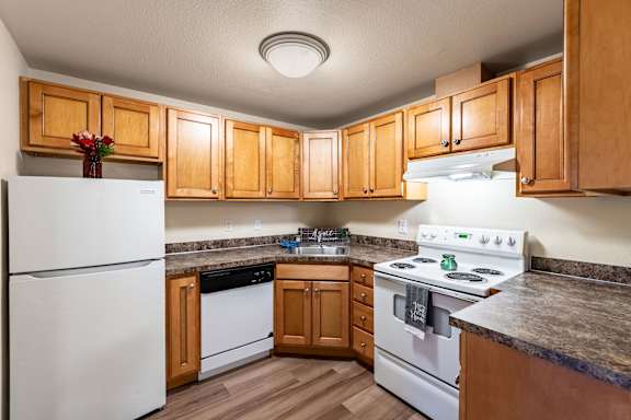 A kitchen with a white refrigerator, a white stove, and wooden cabinets.
