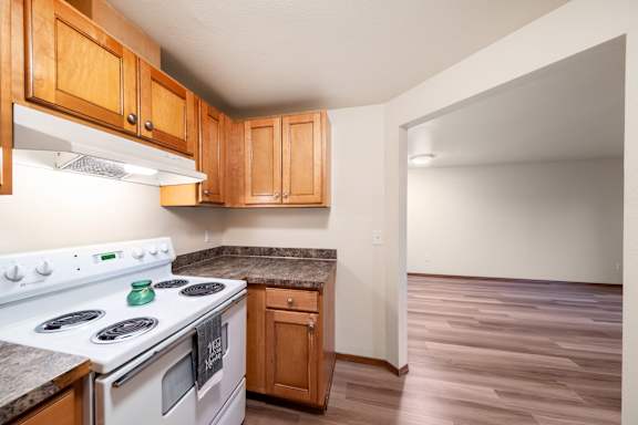 A kitchen with a white stove top oven and wooden cabinets.