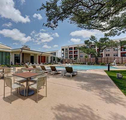 A pool area with a table and chairs in front of a building. at Bridge at Saffron, Austin, TX