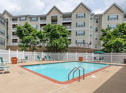 A pool surrounded by chairs and trees in front of apartment buildings.