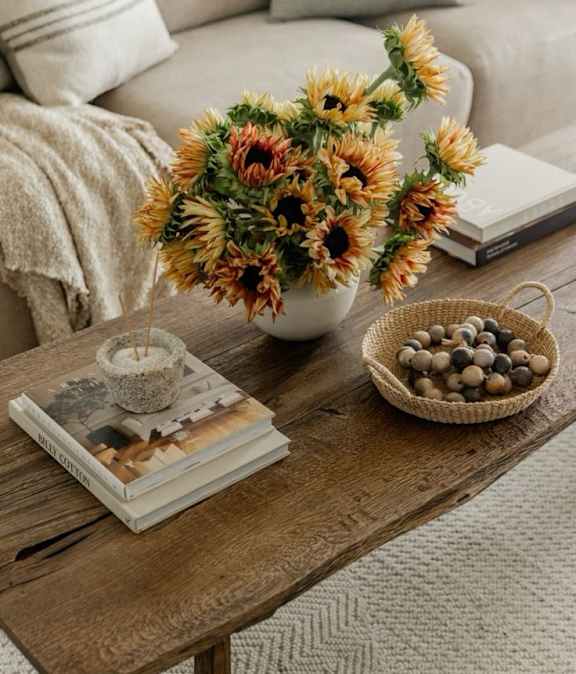 A wooden table with a vase of sunflowers, a book, and a bowl of stones.