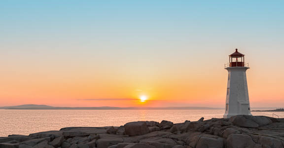 a lighthouse on the rocks with the sun setting over the ocean