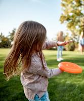 A girl is throwing an orange frisbee in a grassy field.