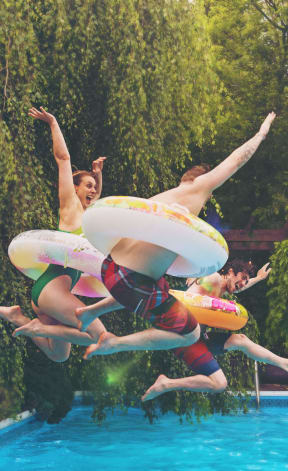 three young men jumping into a swimming pool with frisbees
