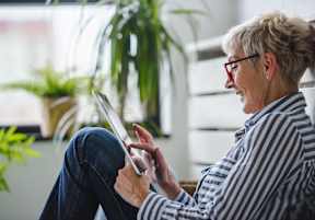 A woman with glasses is using a tablet while sitting on a chair.