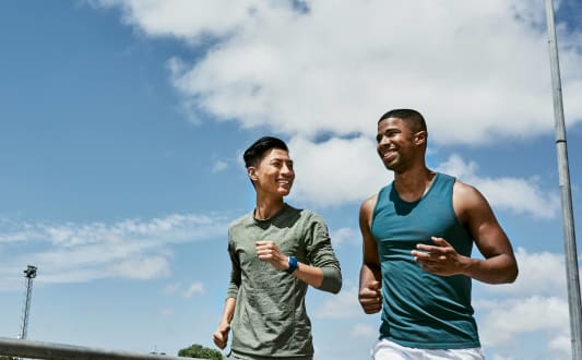 two young men running together outdoors with blue sky at Avenue Two Apartments, Redwood City
