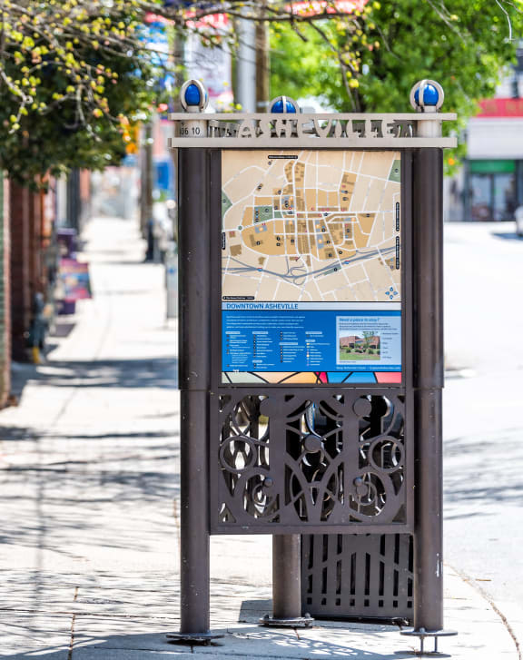 A bus stop sign displaying a map of Asheville, positioned on the side of a street.