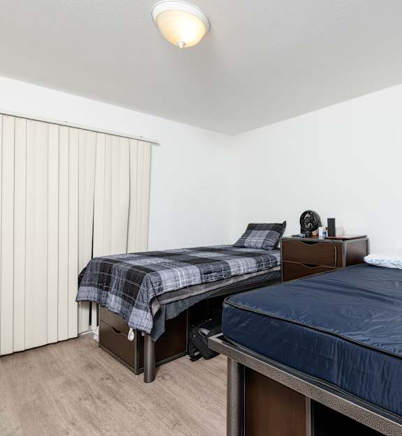 A bedroom with a bed, nightstand, and window with blinds.