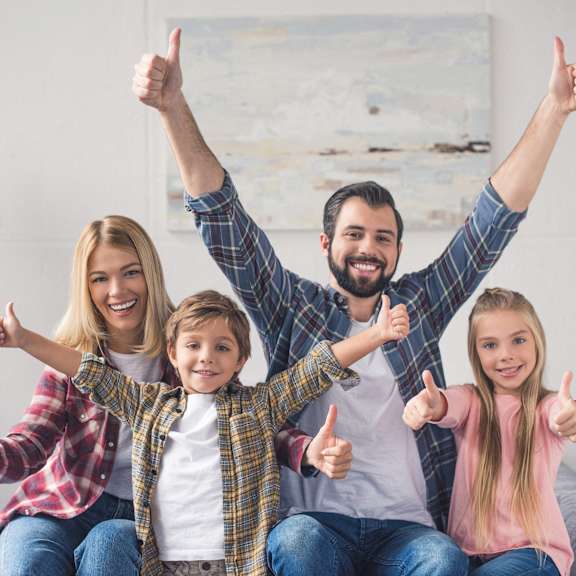 a happy family sitting on a couch with their thumbs up