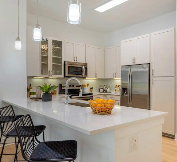A kitchen with white cabinets and a white countertop with a basket of fruit on it.