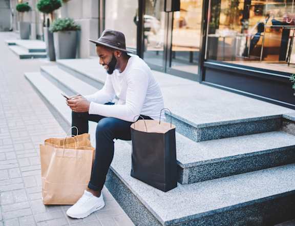 A man sitting on steps with a bag and looking at his phone.
