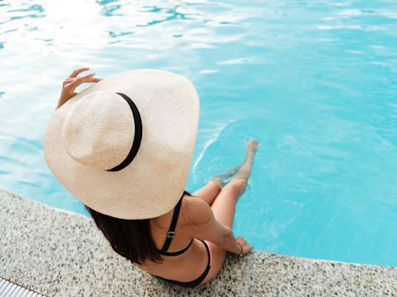 A woman in a hat is sitting by a pool.