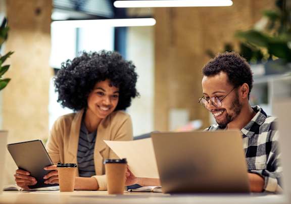 Two people are working on laptops in a well-lit room.
