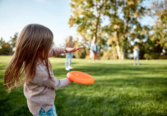 A girl is throwing an orange frisbee in a grassy field.