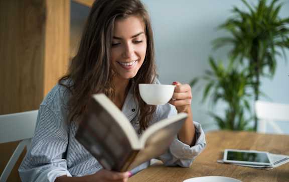 A woman is reading a book while holding a cup of coffee.