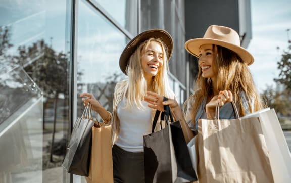two women holding shopping bags and looking at a store window