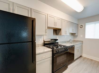 A black refrigerator sits in a kitchen with white cabinets.