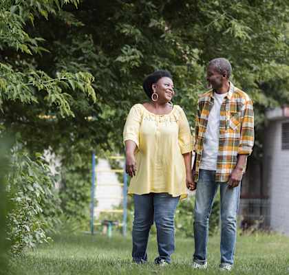 A man and woman are standing in a grassy area under a tree.