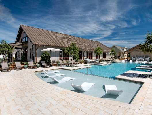 a large swimming pool with lounge chairs and umbrellas in front of a house